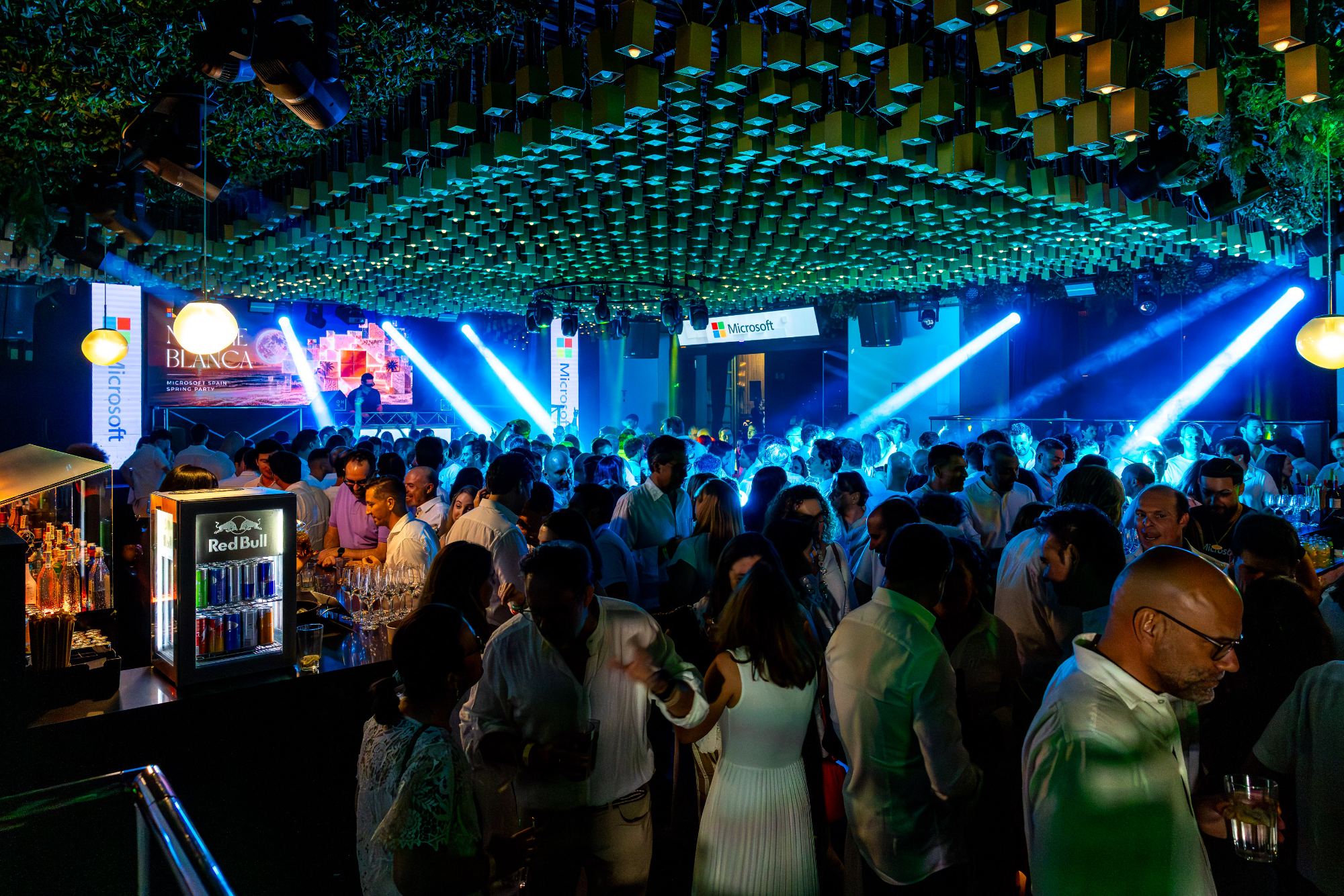 Fiesta corporativa con los asistentes reunidos ante la cabina del DJ y la barra