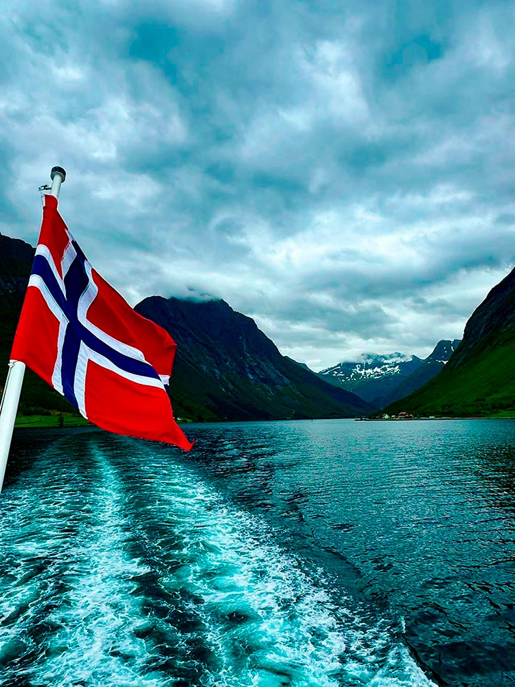 Bandera noruega en la popa de un barco navegando por un fiordo