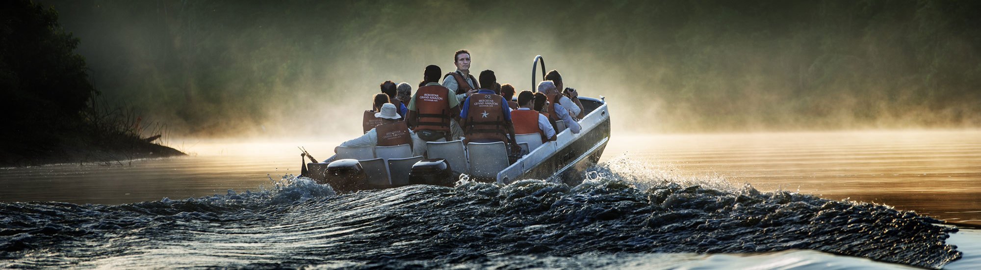 Grupo navegando en lancha por un río entre la niebla al amanecer